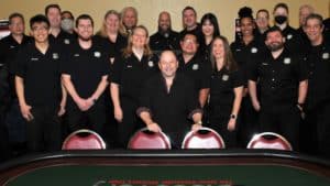 Jason Alexander and The Poker People posing behind a poker table.