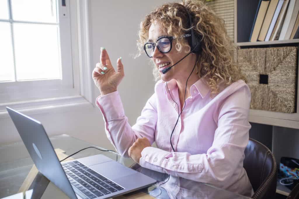 A woman wearing a pick shirt and headset at her desk on a video conference call.