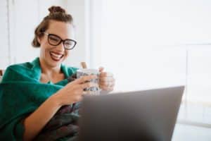 Smiling woman in a green top, holding a coffee mug and looking at her laptop.